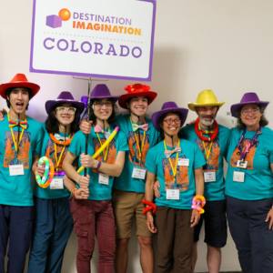 Kate Donelan (far right), Affiliate Director of Destination Imagination (DI) Colorado, poses with a DI Colorado team at Global Finals 2024. They are all wearing matching aqua-colored DI Colorado t-shirts and wearing colorful cowboy hats. 