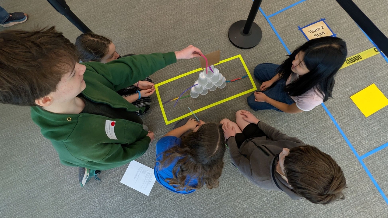 Four students building a barrier with plastic cups and other materials