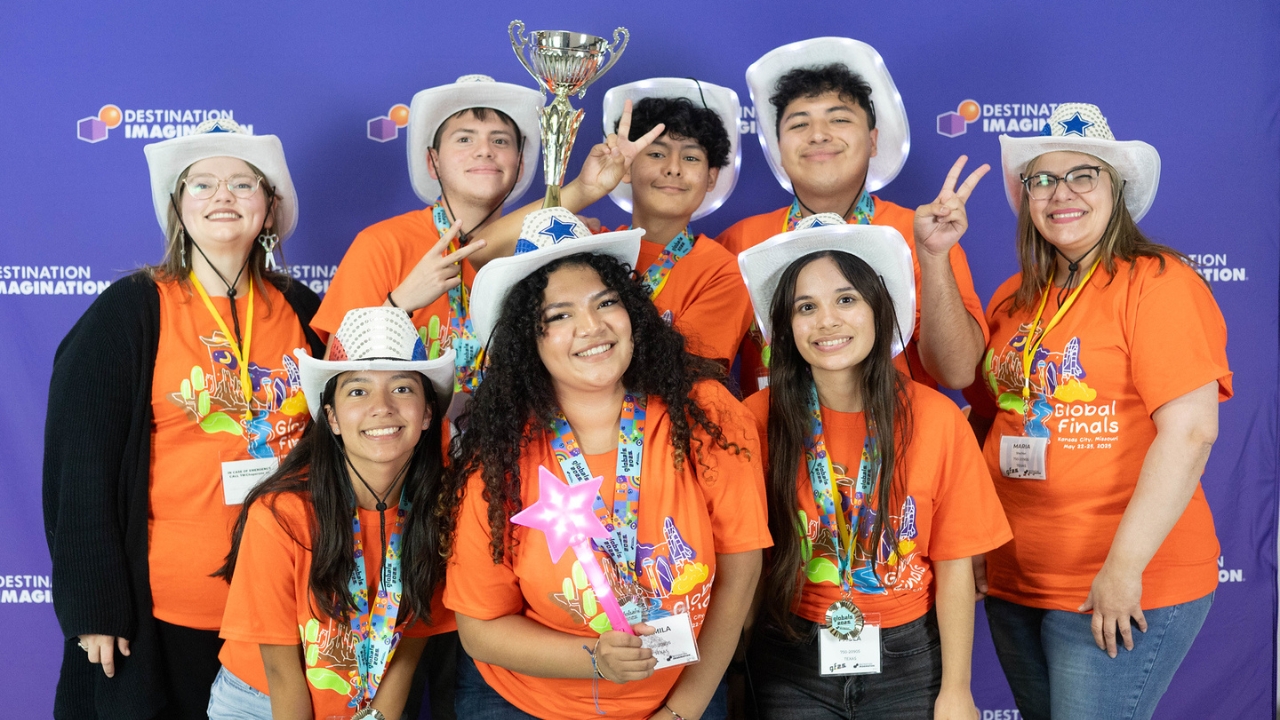 A Destination Imagination team from Texas wearing matching orange t-shirts and posing for a photo with their trophy at Global Finals 2025.