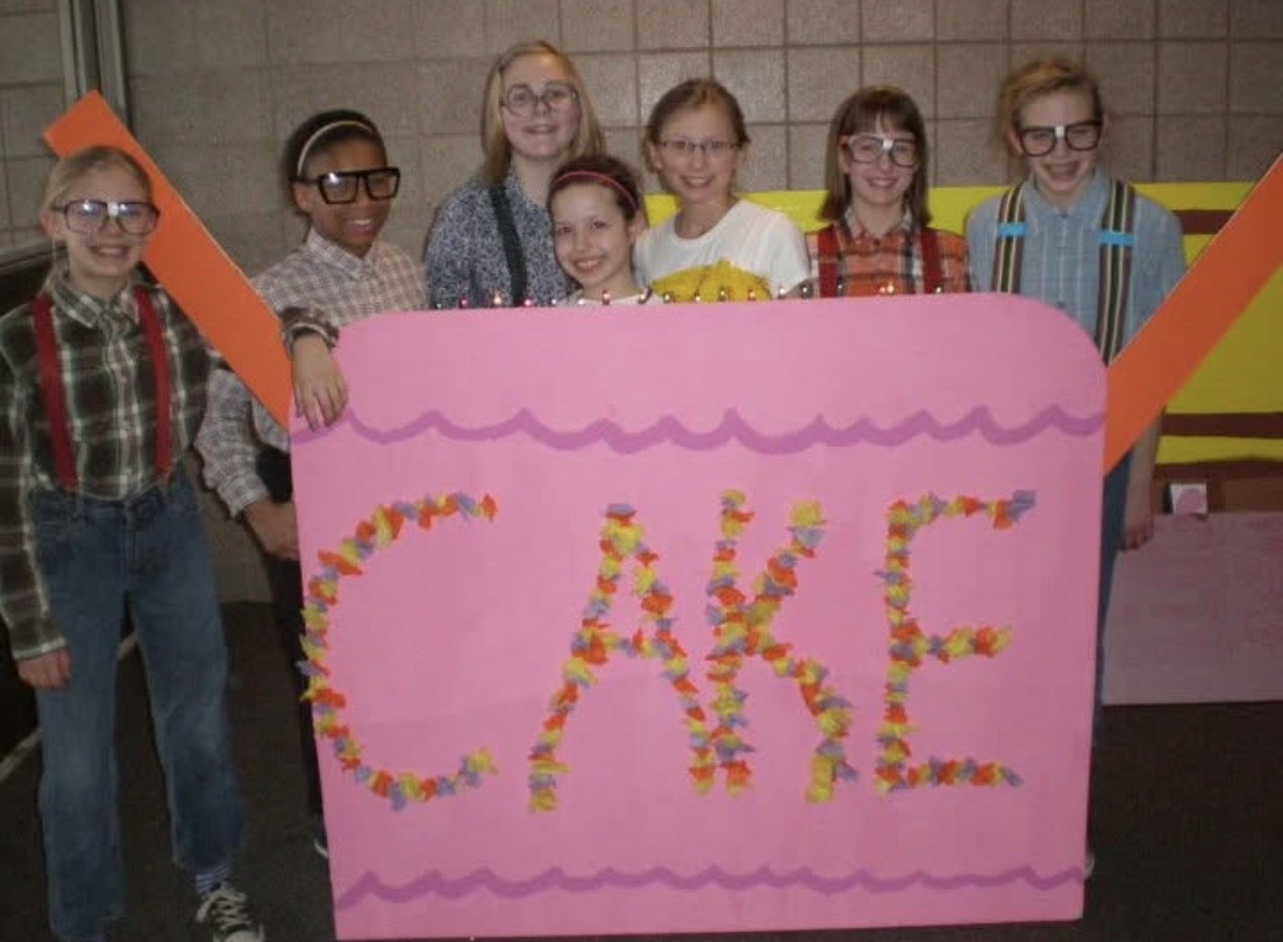 Leah and her Destination Imagination team pose together behind their large pink CAKE prop at a 2012 DI tournament.