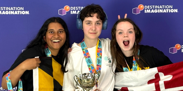 DI team, Ride or D.I., pose for a photo holding their Global Finals 2025 trophy and a large Maryland state flag. 