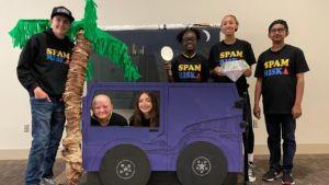 A Destination Imagination team poses with their large, hand-made props for their team presentation, including a palm tree and a bus.