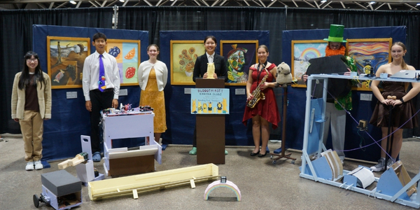 DI team, The Blood-Thirsty Banana Slugs, in costume and standing in front of their backdrop and props for their presentation at Global Finals 2025. 