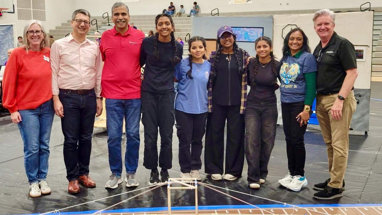 Emily Duke, Texas Affiliate Director (far left), and Destination Imagination CEO Mark Giordono (second from left) stand with a Destination Imagination team and volunteers behind a student-built engineering challenge structure at a Texas tournament, with DI Director of Education Johnny Wells on the far right.